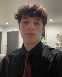 a young man in a black shirt and red tie looking at the camera while standing in a living room