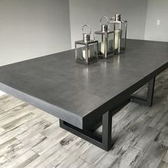 a table with four candles on it in front of a gray wall and wood floor