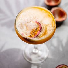 a close up of a drink in a wine glass with fruit on the table behind it