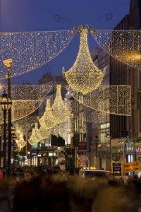 people are walking down the street covered in christmas lights