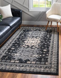 a living room area with black leather couches and rugs on the hardwood floor