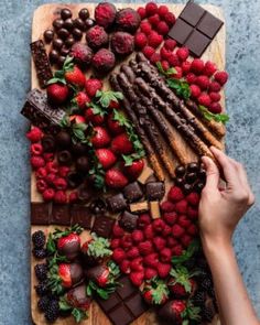 a person is cutting strawberries and chocolate on a wooden board with other food items