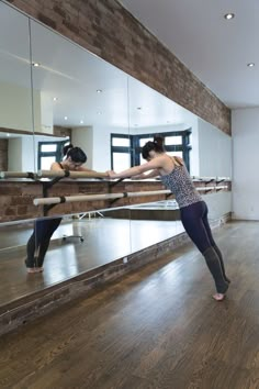 two women are practicing ballet moves in an empty room with mirrors on the wall and hardwood floors