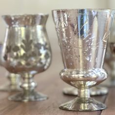 three glass goblets sitting on top of a wooden table next to each other