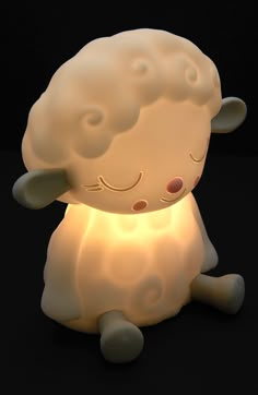 a white sheep lamp sitting on top of a black surface with its eyes closed and it's head turned to the side