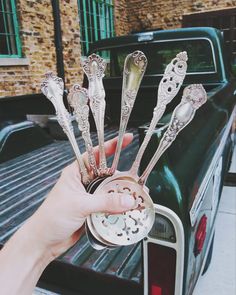 a person holding spoons in the back of a pick up truck with other silverware on it