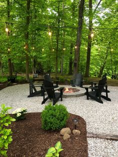 an outdoor fire pit surrounded by chairs and lights in the middle of a wooded area