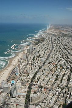 an aerial view of a city next to the ocean with buildings and beach in the foreground