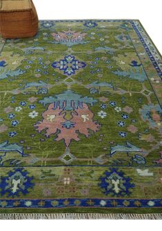 a green rug with blue, pink and orange designs on the ground next to a wooden chair