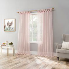 a living room with pink curtains and a white chair in front of a large window