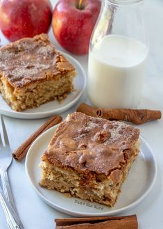 two white plates topped with slices of cake next to a glass of milk and cinnamon sticks