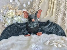 a stuffed animal bat sitting on top of a white fur covered chair next to flowers