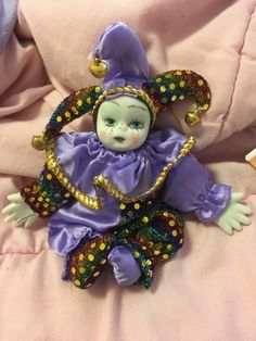 a doll is laying down on a pink blanket and wearing a purple dress with gold accents