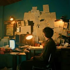 a person sitting at a desk in front of a computer monitor and lamp with papers all over it