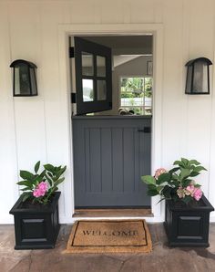 two black planters with pink flowers are on the front steps of a white house