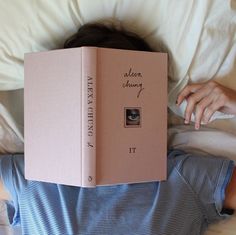 a person laying in bed with a pink book over their head and the cover is open