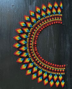 a colorful piece of art made out of beads on a black surface with a circular hole in the middle