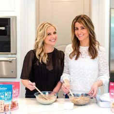 two women standing in a kitchen preparing food on top of a white counter with milk and yogurt