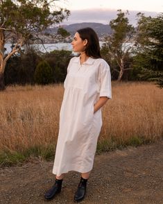 a woman standing in the middle of a field wearing a white dress and black boots