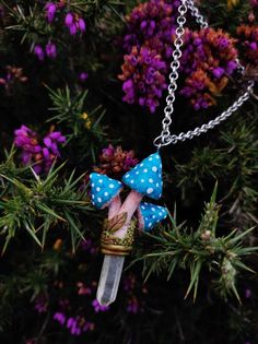 a necklace with a blue bow on it is hanging from a chain in front of purple flowers