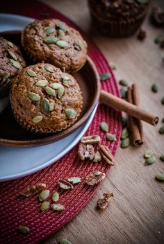 three muffins on a plate with nuts and cinnamon sticks next to them in the background