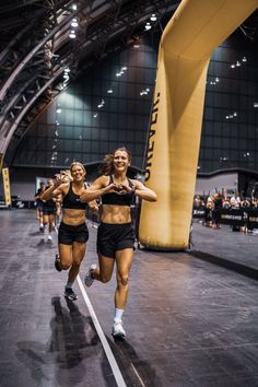 two women running on a race track in the middle of an indoor arena with people watching