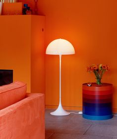 a living room with an orange wall and white floor lamp next to a red couch