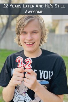 a young boy is holding up two red and white numbers with the words 22 years later and he's still awesome