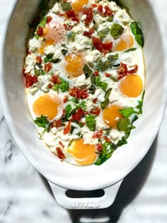 an overhead view of eggs and spinach in a white bowl on a marble surface