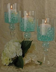 three glass vases with candles and flowers in them