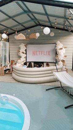 people are sitting in chairs near a pool with a large screen on the wall behind them