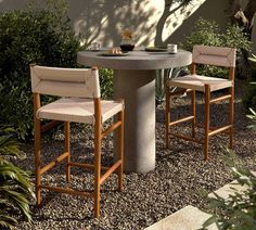 two chairs sitting at a table in the middle of a graveled area next to plants