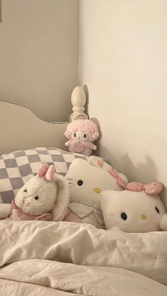 several stuffed animals are on the bed with white sheets and checkerboard wall behind them