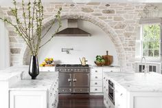 a kitchen with white cabinets and marble counter tops, an arched doorway leading to the outside