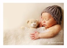 a baby sleeping next to a teddy bear wearing a knitted hat and holding it's head