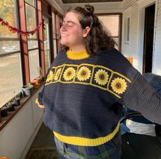 a woman wearing a sweater that has sunflowers on it and is standing in front of a window