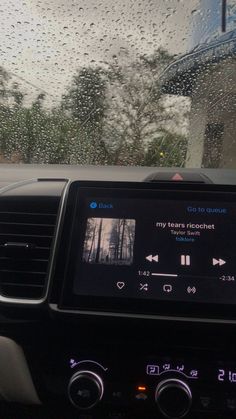 the dashboard of a car with raindrops and trees in the backgroud