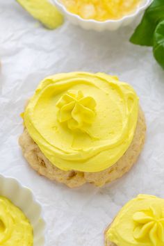 some cookies with yellow frosting on them next to small bowls of butter and leaves