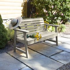 a wooden bench with a hat on it and flowers in the back ground next to it