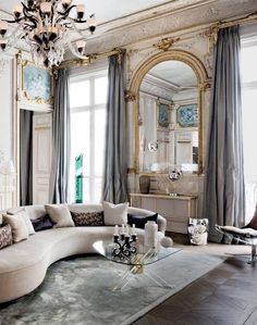 an elegant living room with chandelier, couch and large mirror in the corner