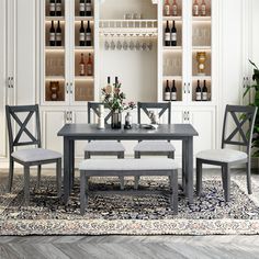 a dining room table and chairs with wine bottles on the shelves behind it in front of an area rug