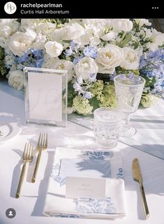 the table is set with white and blue flowers, silverware, and napkins