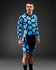 a man wearing a blue and black cycling suit with circles on it, standing in front of a gray background