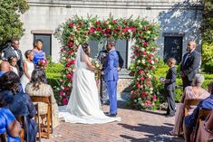 a bride and groom are getting married in front of an arch decorated with red roses