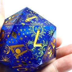 a hand holding a blue dice with gold numbers and stars on the side, in front of a white background