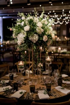 a tall vase filled with white flowers sitting on top of a table covered in wine glasses