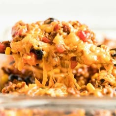 a spoon full of cheesy ground beef casserole is being lifted from the casserole dish