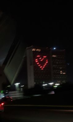 a red heart is projected on the side of a tall building at night with other buildings in the background