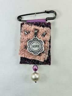 a piece of fabric hanging from a hook on a white wall with a beaded ball attached to it