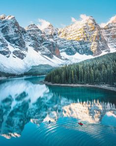 two kayakers paddling in the calm waters of a lake surrounded by snow covered mountains